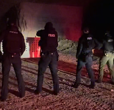 Four police officers in tactical uniforms viewed from behind conducting night training at PTF's subterranean firing range.